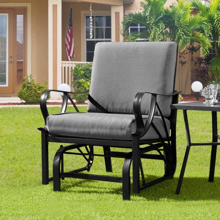 Patio glider rocking chair with gray thick cushion and curved armrests, perfect for outdoor relaxation.