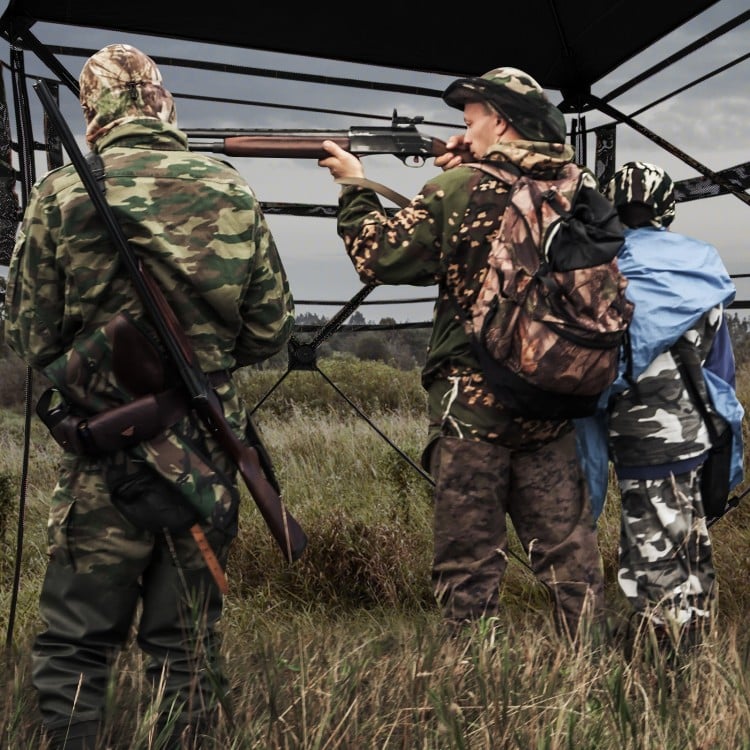 Hunting blind with camouflage pattern, 82" tall, accommodates 3-4 people, featuring one-way see-through panels for.