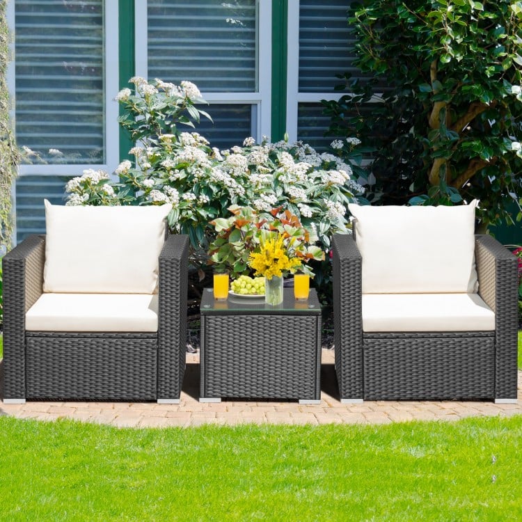 Two wicker patio chairs with white cushions and a glass-top table, perfect for outdoor relaxation in the garden.