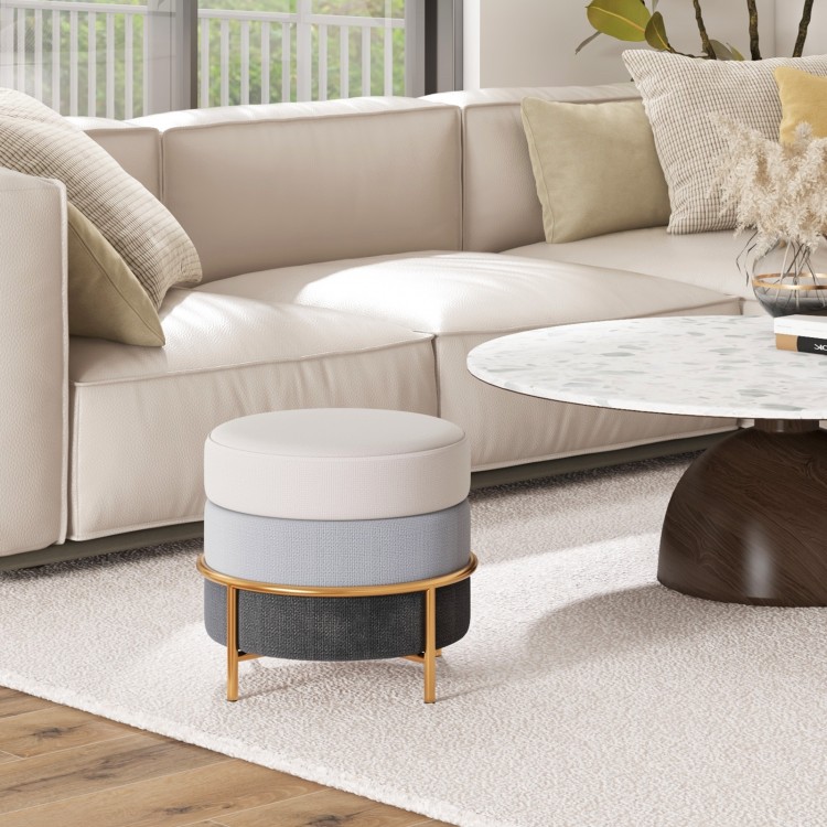 Round upholstered ottoman in gray with gold metal legs, ideal as a footrest or side table for living room use.