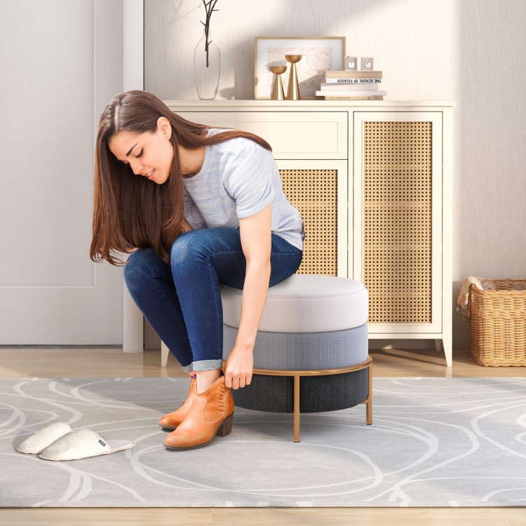 Round upholstered ottoman in gray with gold metal legs, serving as a footrest and vanity stool for versatile use.