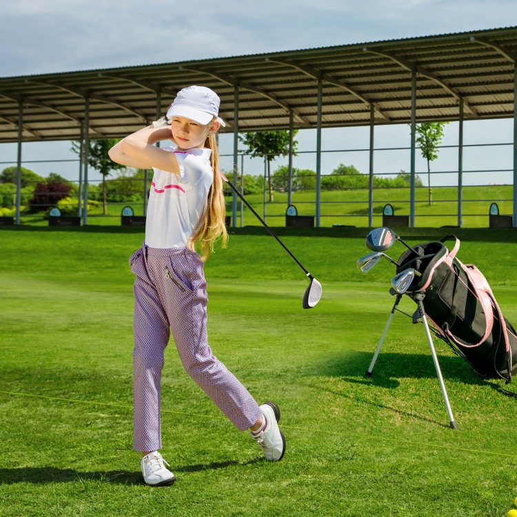 Junior golfer swinging a club, wearing a pink outfit, with a complete golf club set and stand bag on the course.