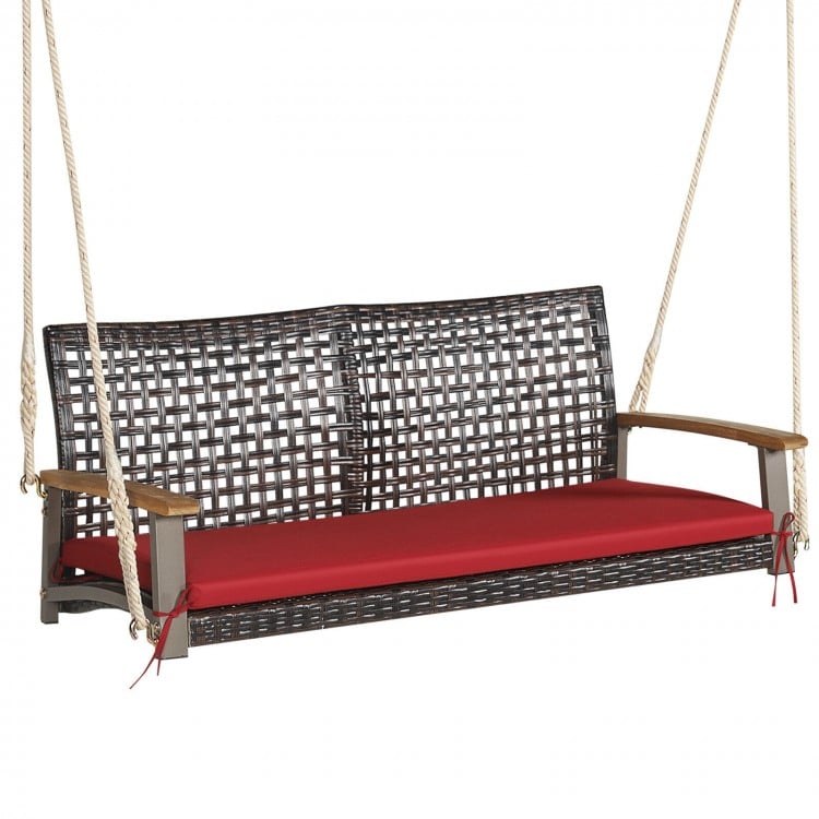 Rattan hanging porch swing chair for 2 with red cushion, acacia wood armrests, and sturdy steel frame for outdoor use.