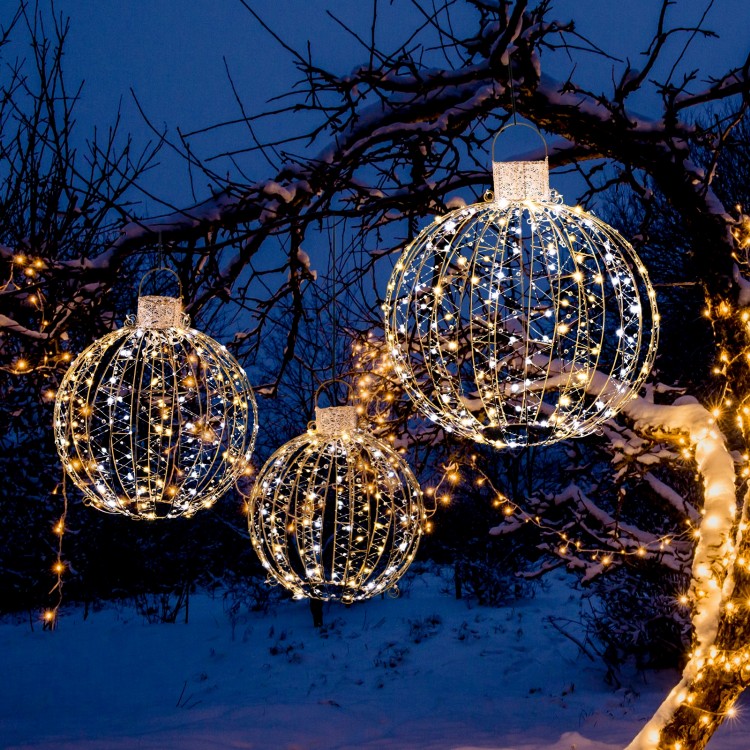 Three decorative Christmas LED light balls in golden hues, featuring warm and white lights, suspended in a snowy.