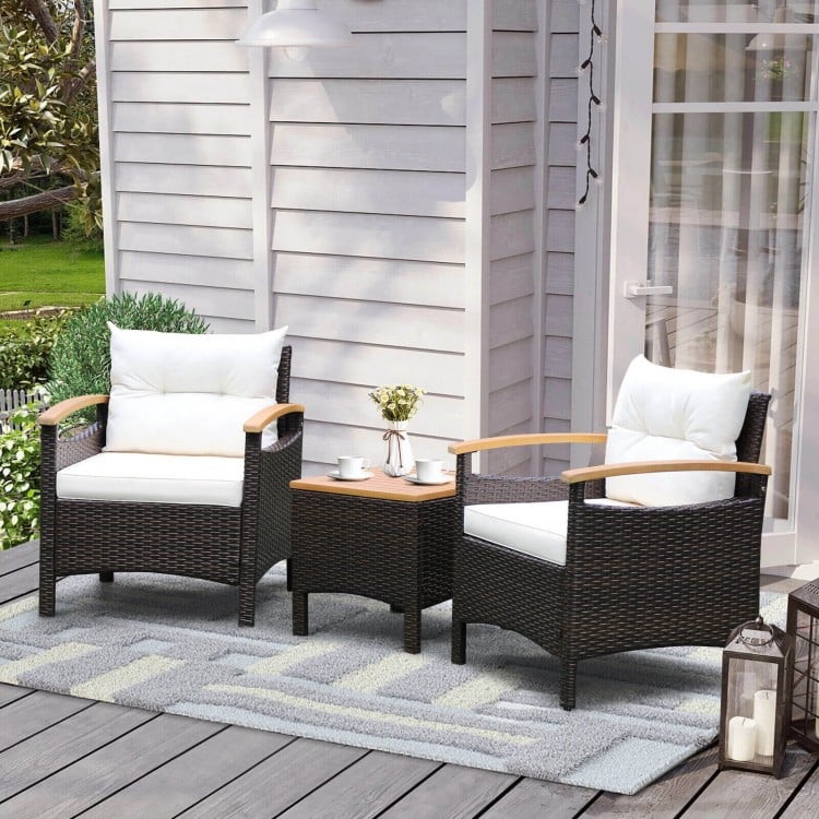 Two chairs with off-white cushions and a brown rattan side table, perfect for outdoor patio relaxation.