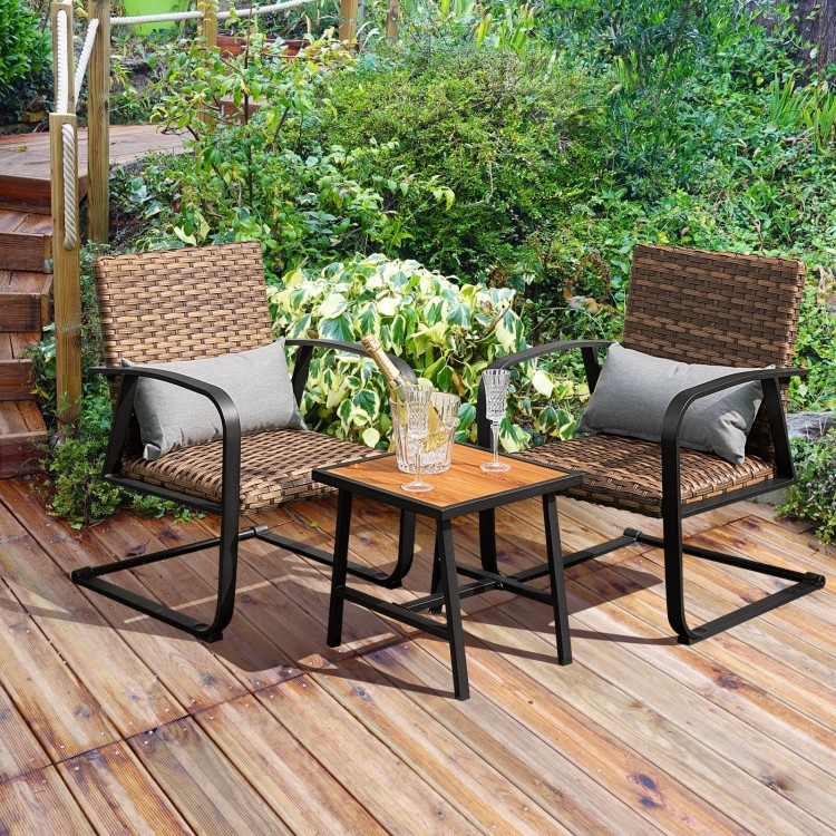 Two rocking chairs with lumbar pillows and a table, made of hand-woven brown PE rattan, perfect for outdoor relaxation.