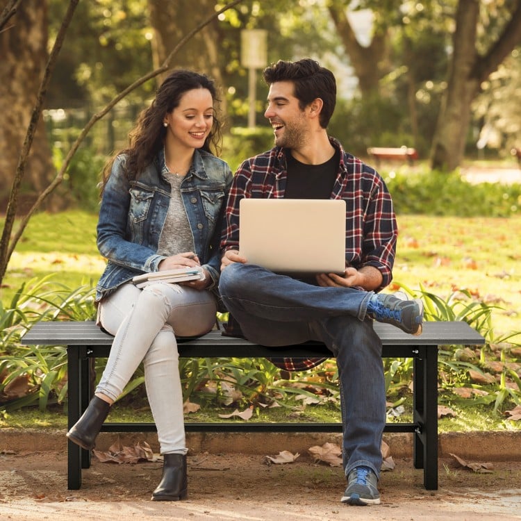 Two people sitting on a 47-inch outdoor bench with a slatted seat, made of weather-resistant HDPE, in a garden setting.
