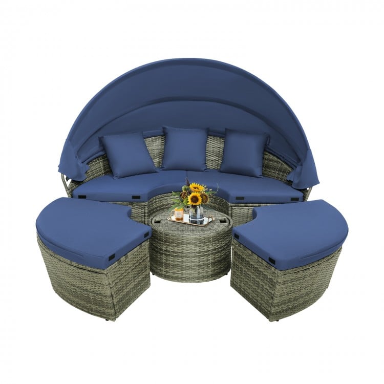 Round outdoor daybed with retractable canopy, navy cushions, and gray PE wicker, perfect for backyard relaxation.