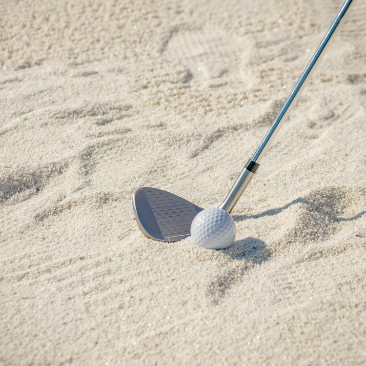 Golf sand wedge with milled grooves and stainless steel head, positioned in sand for improved short game performance.