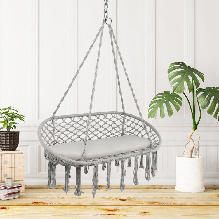 Gray macrame 2-person hammock chair with cushion, featuring bohemian style, suitable for indoor or outdoor relaxation.