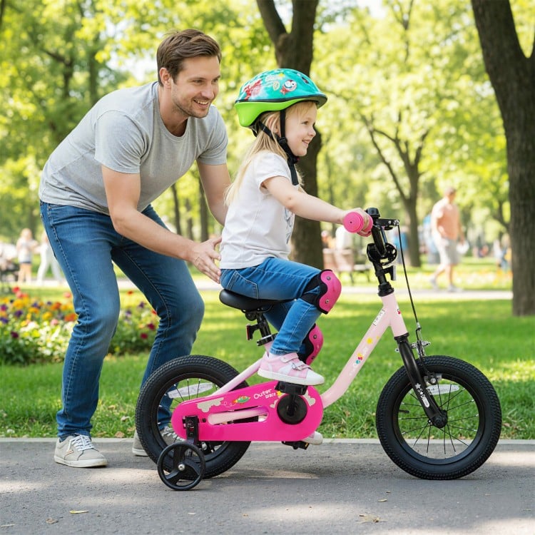 Child riding a pink 12-inch kids bike with training wheels, featuring a dual brake system and ergonomic seat in a park.