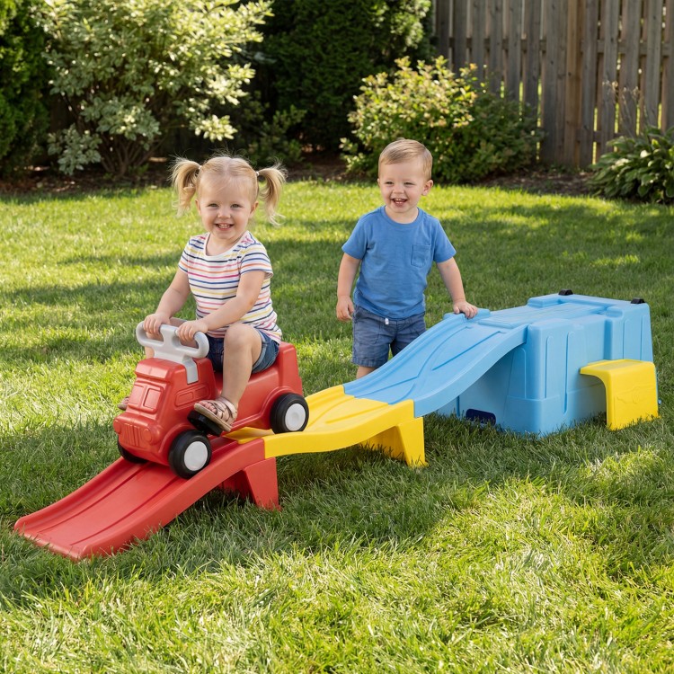 Two toddlers enjoy playing on a multicolor kids ride-on toy with a storage box and downhill race tracks in the backyard.