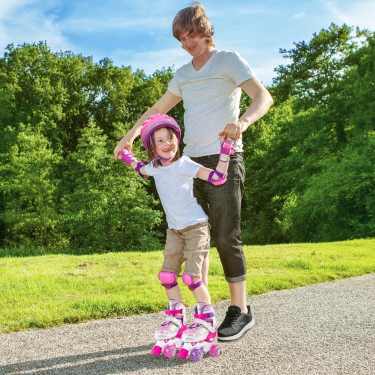 Adjustable kids roller skates in rose red with light-up wheels, safety gear, and a parent assisting on a sunny path.
