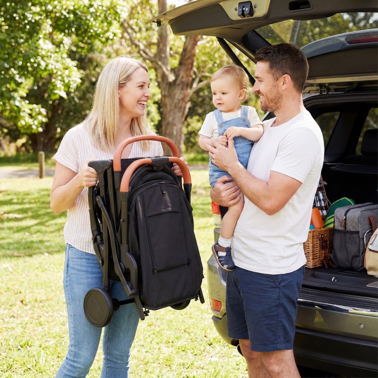 Lightweight black baby stroller with one-hand folding design, shown being carried by a parent for easy transport.
