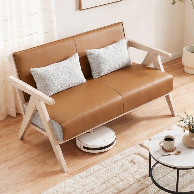 Loveseat sofa in brown artificial leather with gray throw pillows, featuring a rubber wood frame for small spaces.