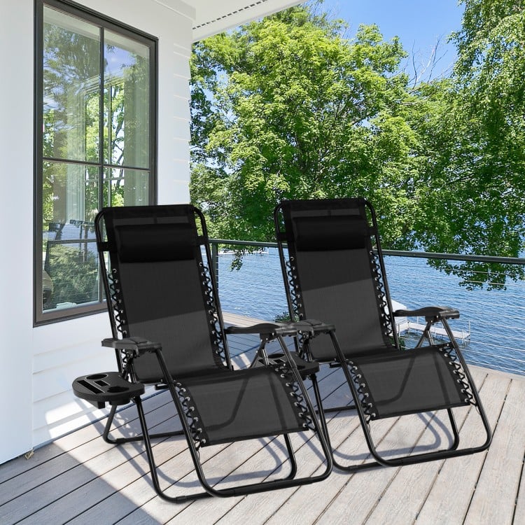 Two black outdoor folding zero gravity reclining lounge chairs with utility tray, perfect for relaxing by the water.