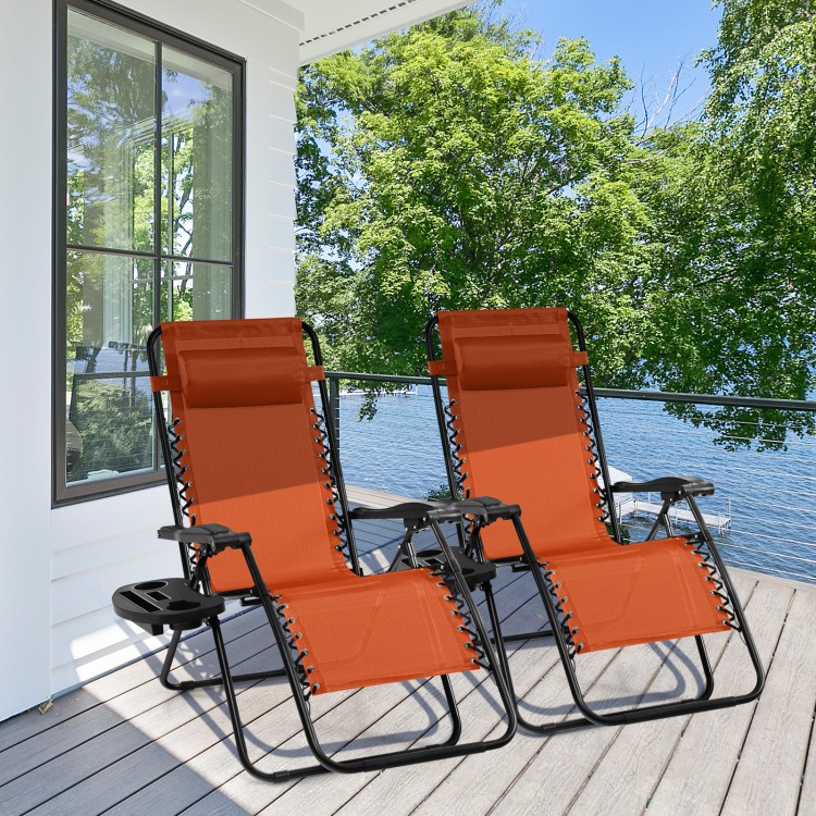 Two outdoor folding zero gravity reclining lounge chairs in orange, featuring adjustable backs and cup holders, perfect.