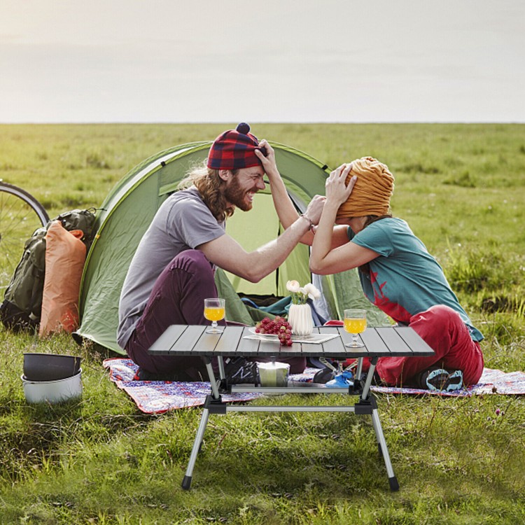 Folding heavy-duty aluminum camping table with adjustable height, set up for picnic in a grassy outdoor setting.
