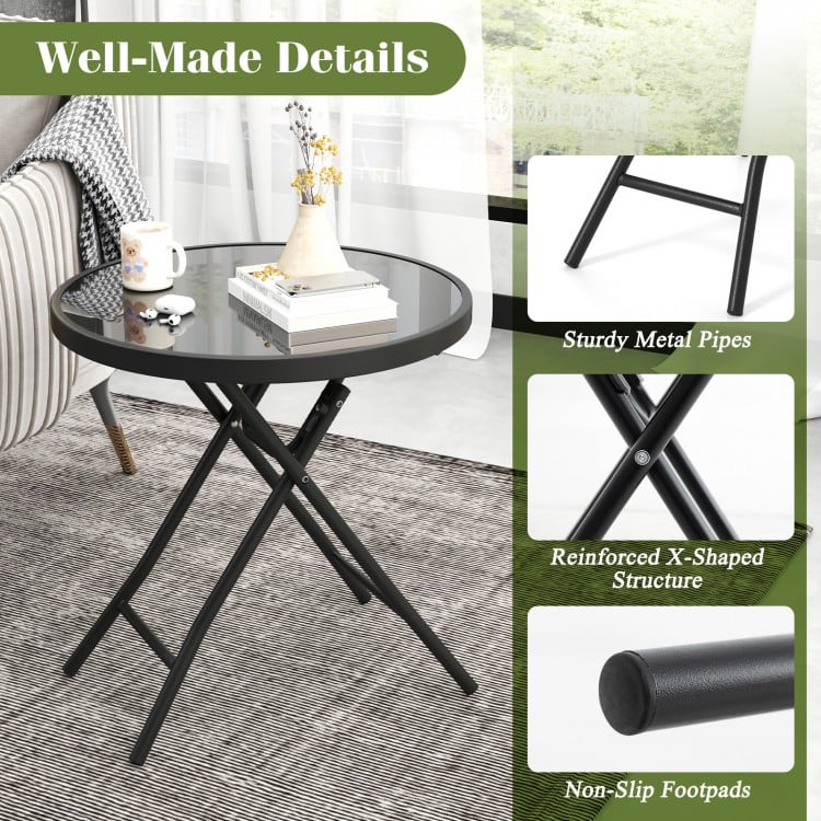 Round black folding side table with tempered glass top and reinforced X-shaped metal frame for indoor and outdoor use.