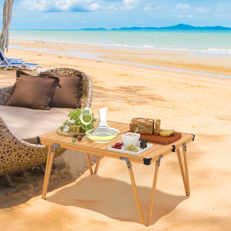 Folding camping table with waterproof surface, set up for a picnic on the beach, featuring a sturdy frame and storage.