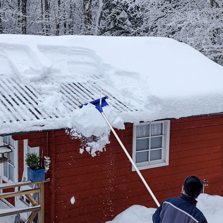 Adjustable 21-foot aluminum snow roof rake with wheels, removing snow from a roof for easy winter maintenance.