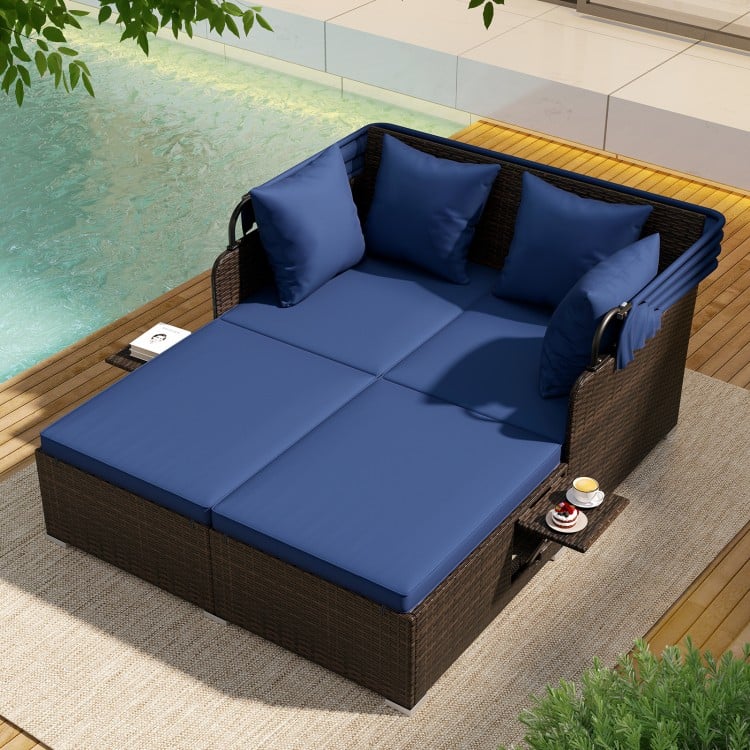 Outdoor patio rattan daybed in navy with soft cushions, retractable canopy, and side tables for poolside relaxation.