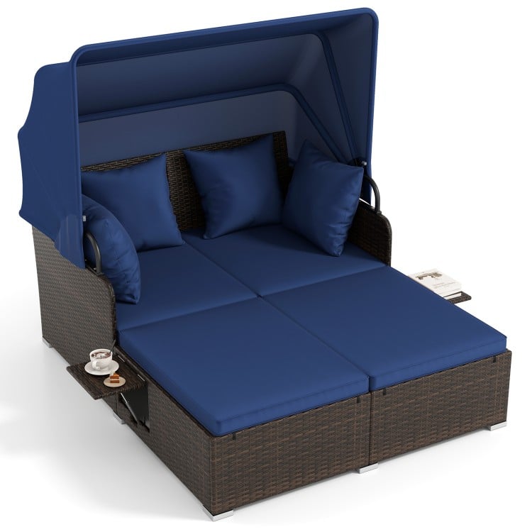 Outdoor patio rattan daybed with retractable canopy and navy cushions, featuring side tables for added convenience.