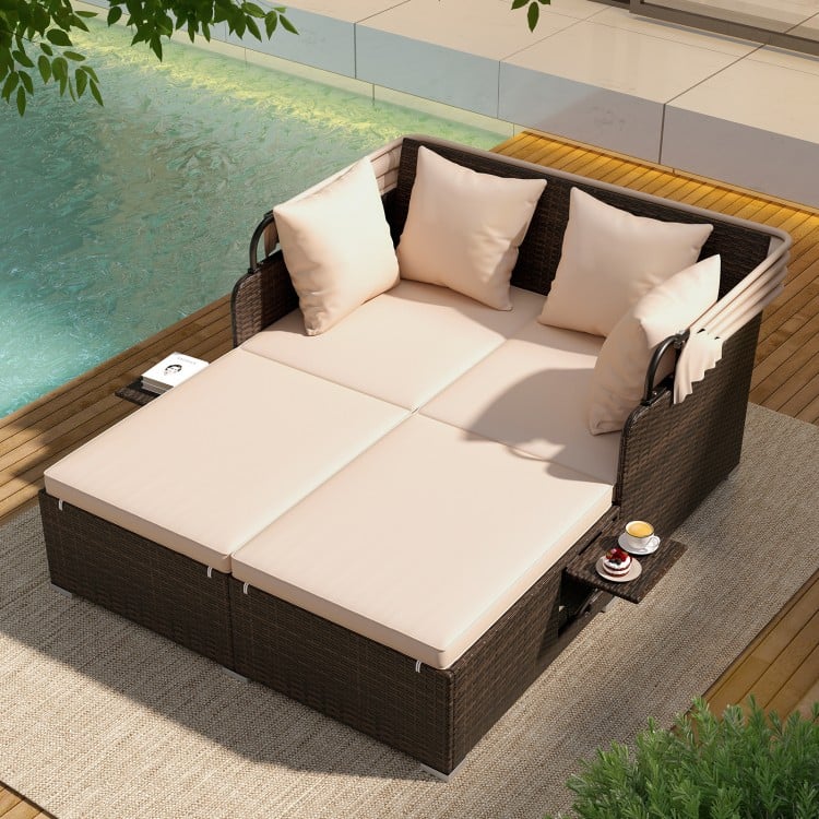 Outdoor patio rattan daybed with beige cushions, retractable canopy, and side tables, perfect for poolside relaxation.
