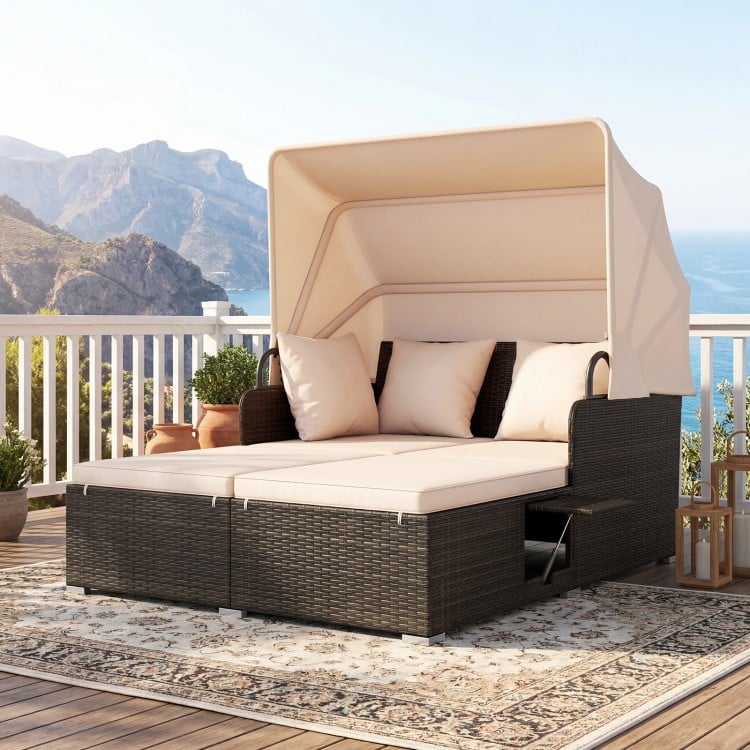 Outdoor patio rattan daybed with beige cushions and retractable canopy, perfect for backyard relaxation by the poolside.