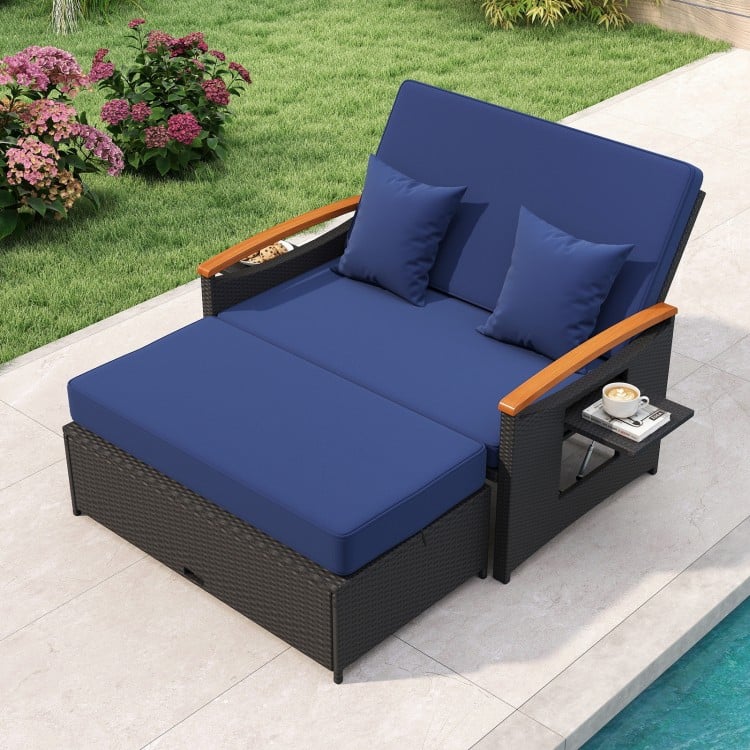 Outdoor wicker daybed with dark blue cushions, adjustable backrest, and storage ottoman for patio relaxation.