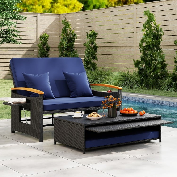 Outdoor wicker daybed with dark blue cushions and folding panels, perfect for patio relaxation and conversation.