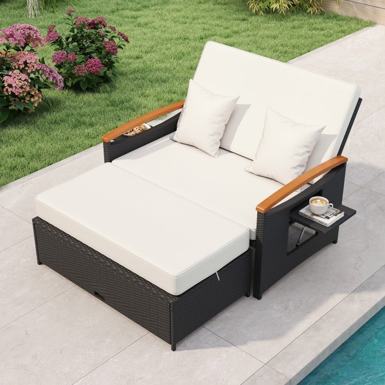 Outdoor wicker daybed with white cushions, adjustable backrest, and storage ottoman for patio relaxation.