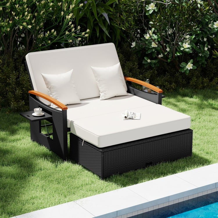 Outdoor wicker daybed with white cushions and wooden armrests, featuring storage ottoman for patio relaxation.