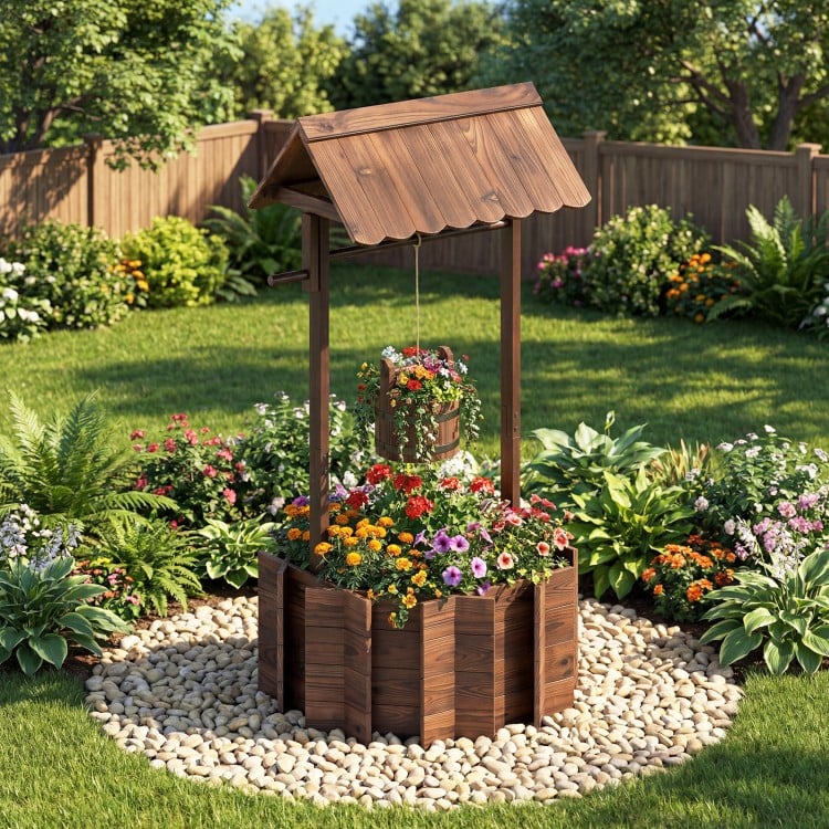 Outdoor wooden wishing well planter with burnt-like finish, featuring a hanging bucket for flowers in a garden setting.