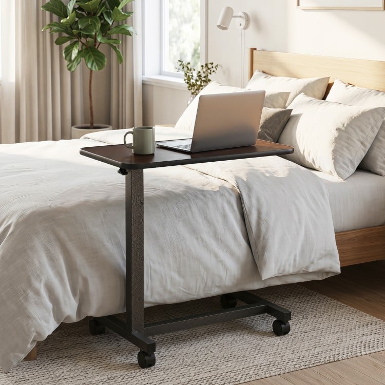 Overbed table in walnut finish with lockable wheels and sturdy H-shaped base, perfect for home or hospital use.