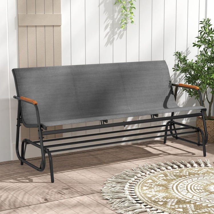 Patio glider bench with curved teak armrests and grey breathable fabric seat, perfect for backyard relaxation.
