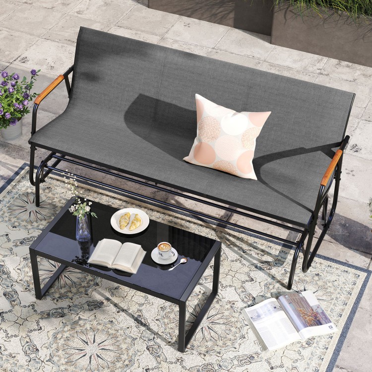 Patio glider bench with teak armrests and breathable grey fabric seat, perfect for backyard relaxation.