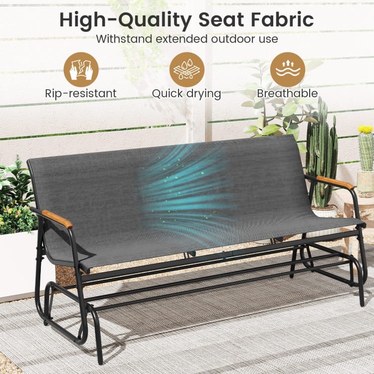 Patio glider bench with curved teak armrests and breathable grey fabric seat, perfect for outdoor relaxation.