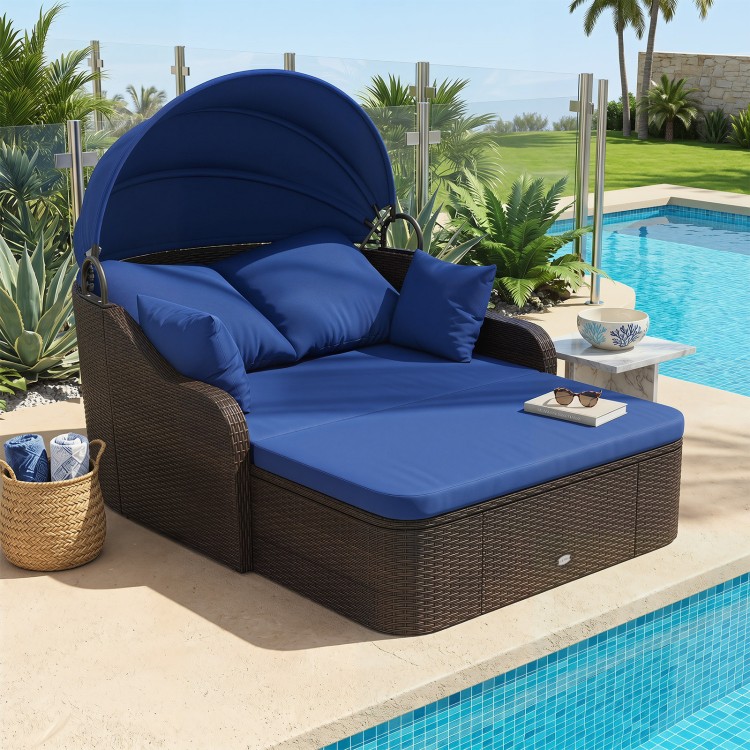 Patio PE rattan daybed with retractable canopy, navy cushions, and four throw pillows, ideal for comfortable outdoor lounging.