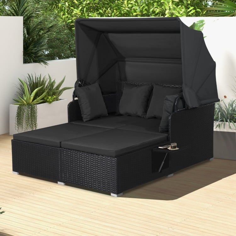 Black patio rattan daybed with retractable canopy and side tables, featuring soft cushions for outdoor relaxation.
