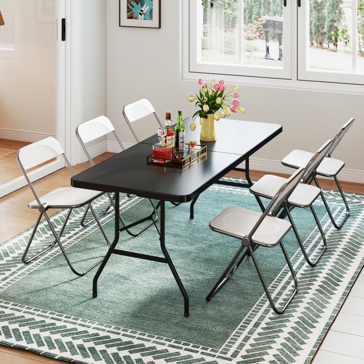 Portable folding camping table in black with a large tabletop, set up for dining in a bright indoor space.