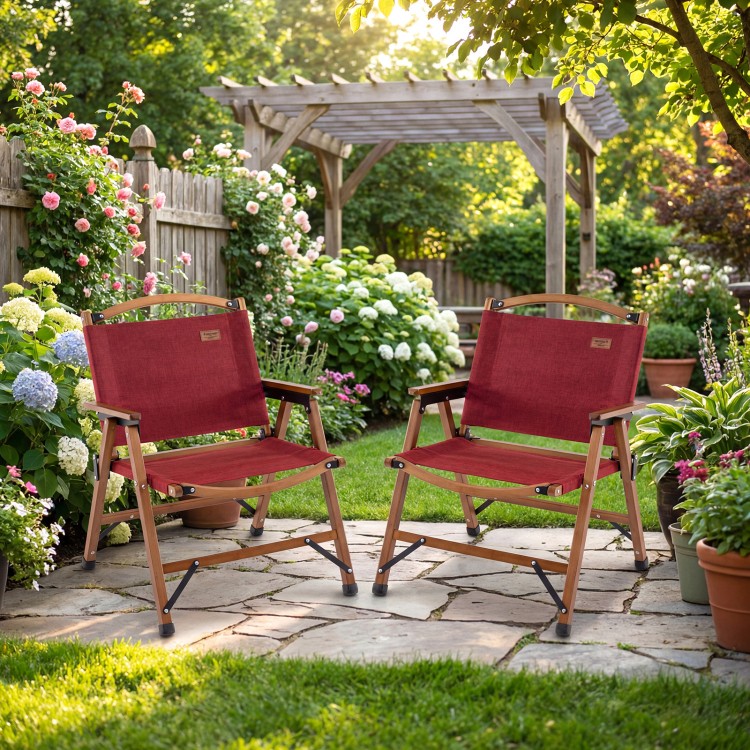 Two red portable folding camping chairs with bamboo frames in a lush garden setting, perfect for outdoor relaxation.