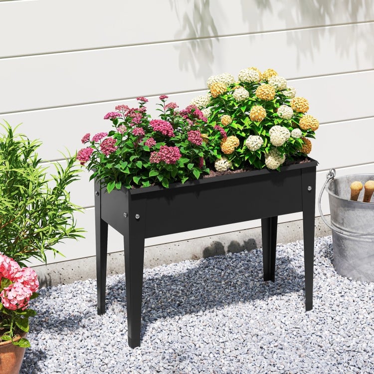 Elevated metal planter box with legs, featuring drainage holes, filled with colorful flowers for outdoor gardening.