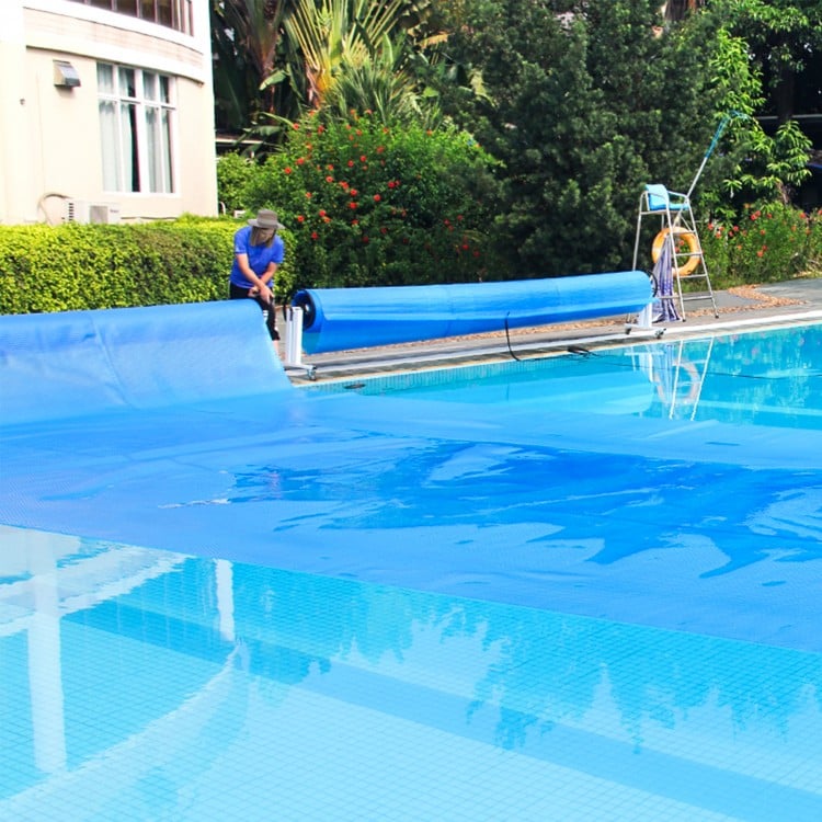 Rectangle swimming pool cover being unrolled, 12-mil thick PE material for heat retention and debris protection.