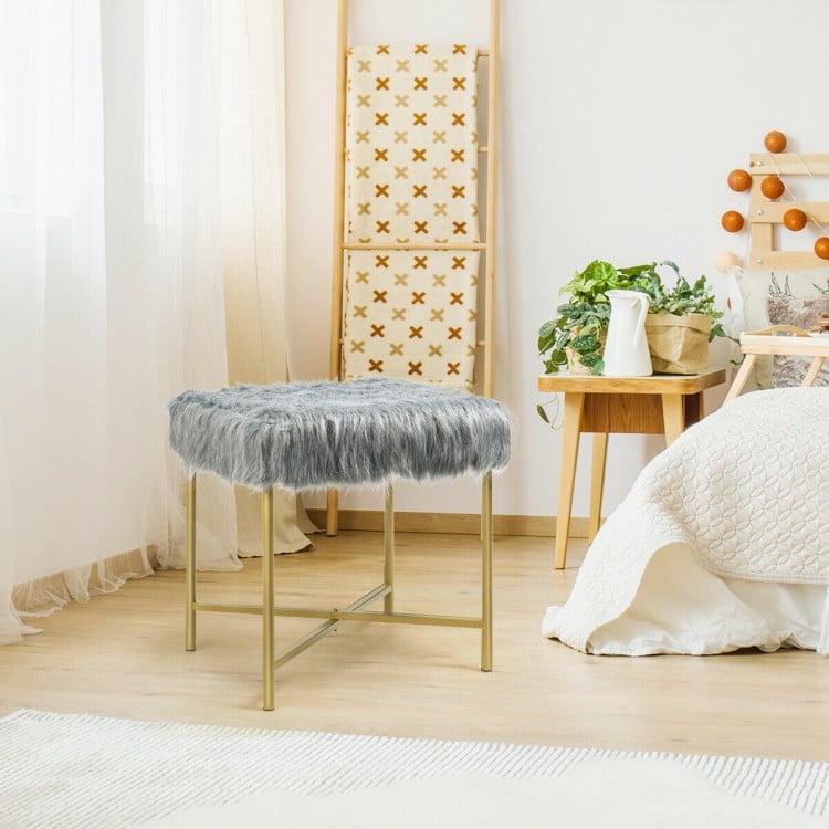 Gray faux fur ottoman stool with golden metal legs, perfect for small spaces and versatile use in any room.