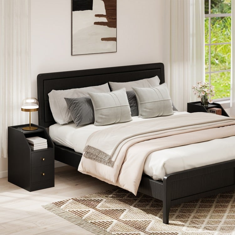 Black side end table with charging station, two drawers, and open compartment for organized storage beside a bed.