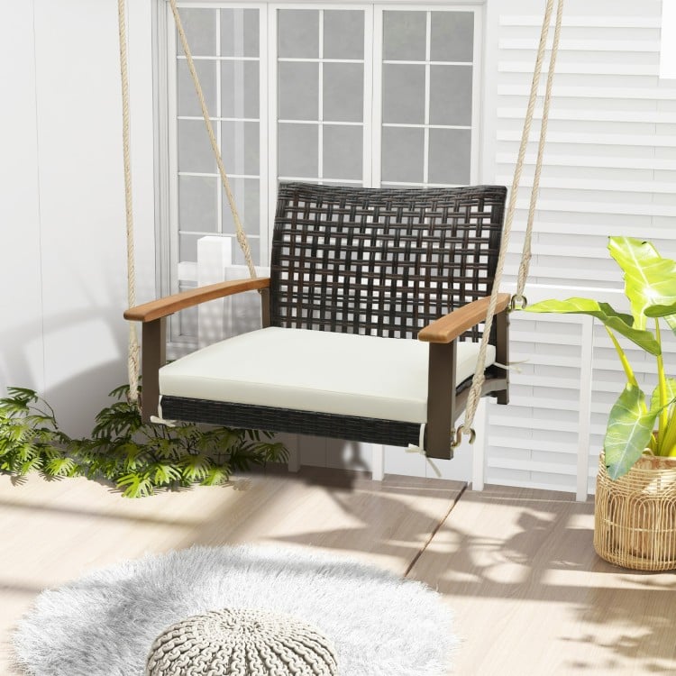 Single rattan porch swing with white cushion, acacia wood armrests, and durable hanging ropes for outdoor relaxation.
