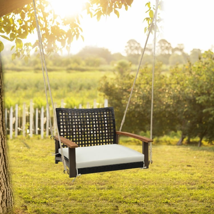 Single rattan porch swing with white cushion and acacia wood armrests, perfect for outdoor relaxation in gardens or.