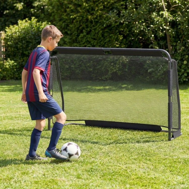 Youth player kicking a soccer ball towards a 6 ft x 4 ft metal frame goal post in a backyard setting.