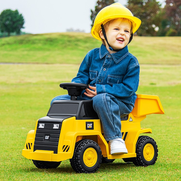 Child riding a yellow 6V electric Caterpillar construction vehicle with a detachable dump bed on grass.
